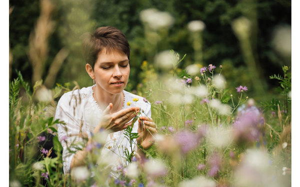 Frau sitzt in Wiese und begutachtet Blume